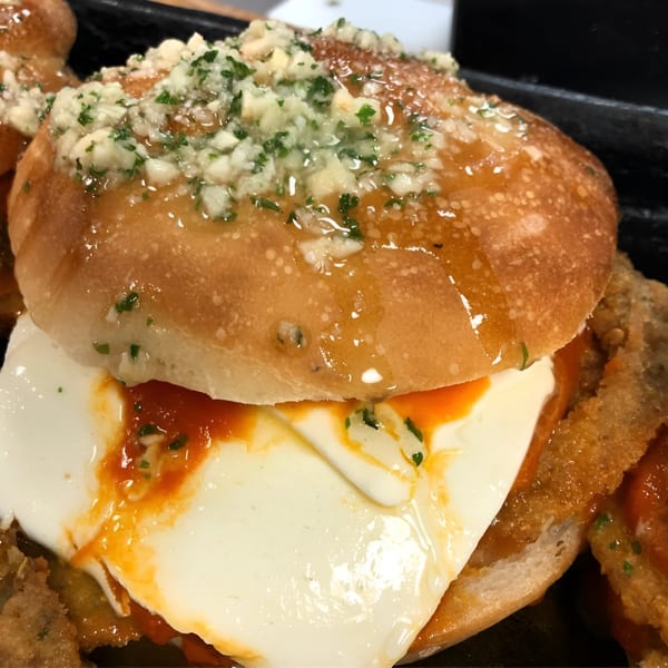 A close-up of a Pino's La Forchetta chicken parmesan slider with melted cheese and sauce.
