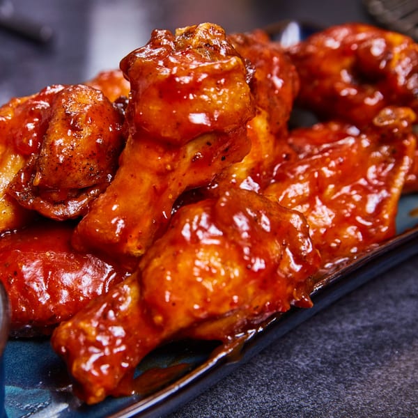 Close-up of several chicken wings coated in a glistening, spicy red sauce on a dark blue plate.