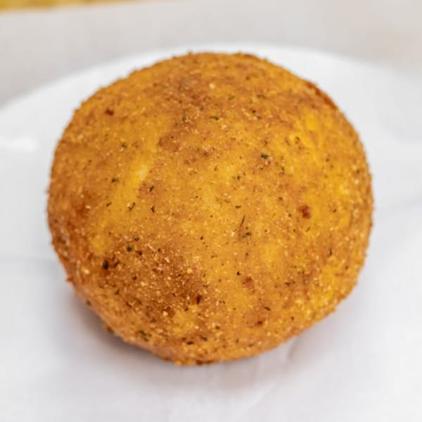 A single, golden-brown arancini, a fried rice ball, sits on a white surface.