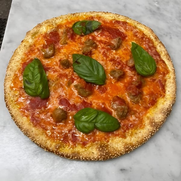 Pino's La Forchetta pizza with tomato sauce, sausage, cheese, and fresh basil on a marble surface.