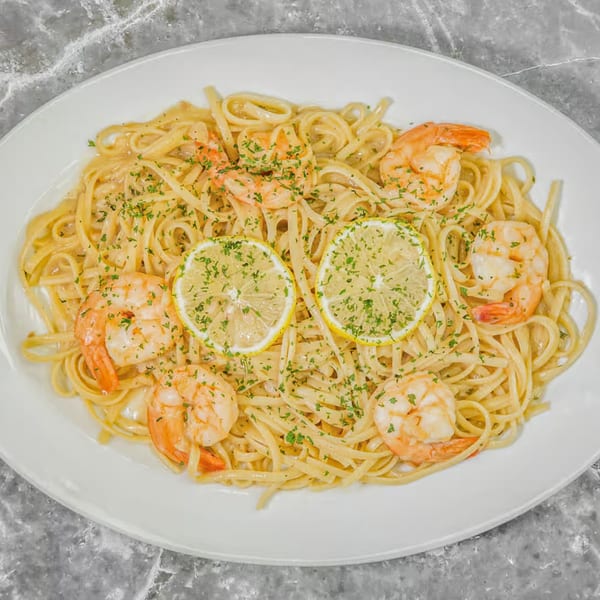 Pino's La Forchetta's shrimp scampi with linguine, parsley, and lemon slices on a white plate.