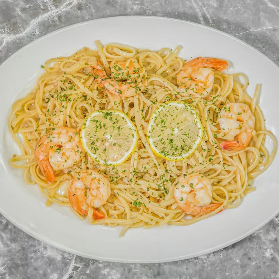 Pino's La Forchetta's shrimp scampi with linguine, parsley, and lemon slices on a white plate.